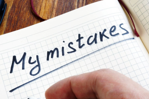 Man's hand, writing in a journal the words My Mistakes as he prepares to list them.