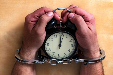 Man in handcuffs holding an alarm clock. Representative of being asked to do something illegal or against his values.