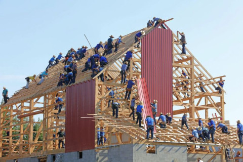 Old fashioned barn raising. Men in blue shirts with hats working together to raise a new barn.